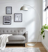 A living room scene with a grey fabric sofa, grey rug and large matt grey metal floor lamp in an arc shape with large domed lampshade. On the wall behind the sofa is 3 framed pictures. A plant and black blinds can be seen to the right of the shot.