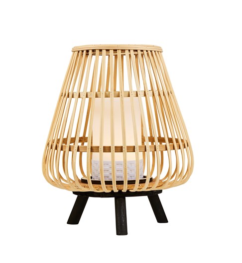 A bamboo cage style lantern style table lamp stood on a black coloured tripod base. The lantern has a white plastic pillar candle style central piece which houses a battery powered LED bulb. The central light is turned on in this picture.