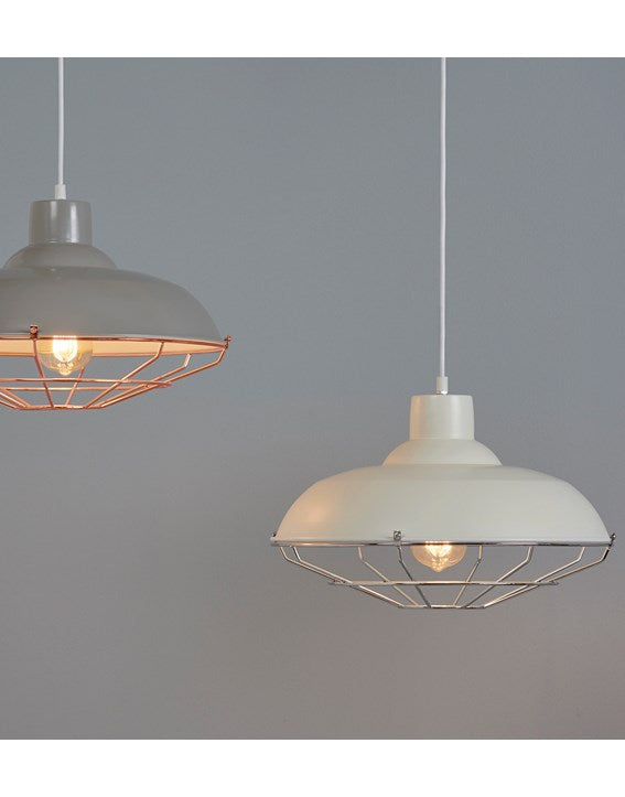 A pale grey background and a cream painted metal lampshade with a silver coloured thin metal cage surrounding an illuminated bulb, to the left of the picture a grey painted version with copper coloured metal wire can be seen.